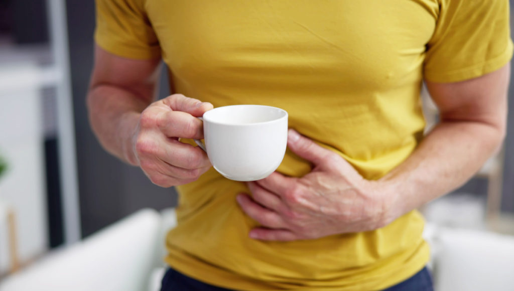 Featured image for this post on Which Coffee Is Less Acidic, showing a man with heartburn holding a cup of coffee