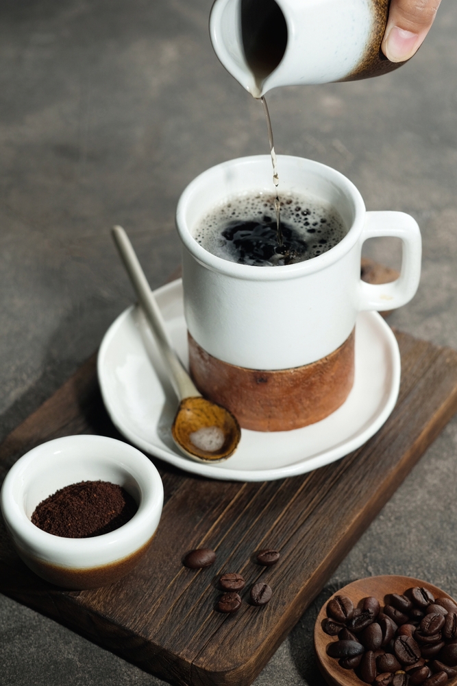 a cup of instant coffee. The cup is white and someone is pouring hot water into the cup with the coffee powder