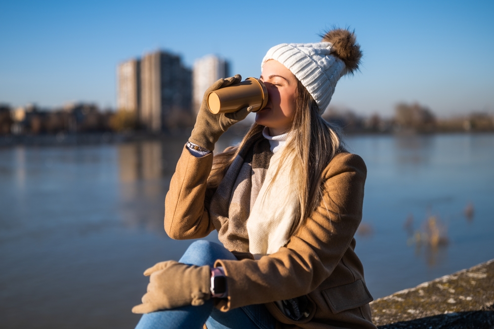 A woman enjoying a coffee a chill morning along the beasch. Hamilton Beach FlexBrew Trio 2-Way Review can give you an idea if you should choose this to get the same feeling